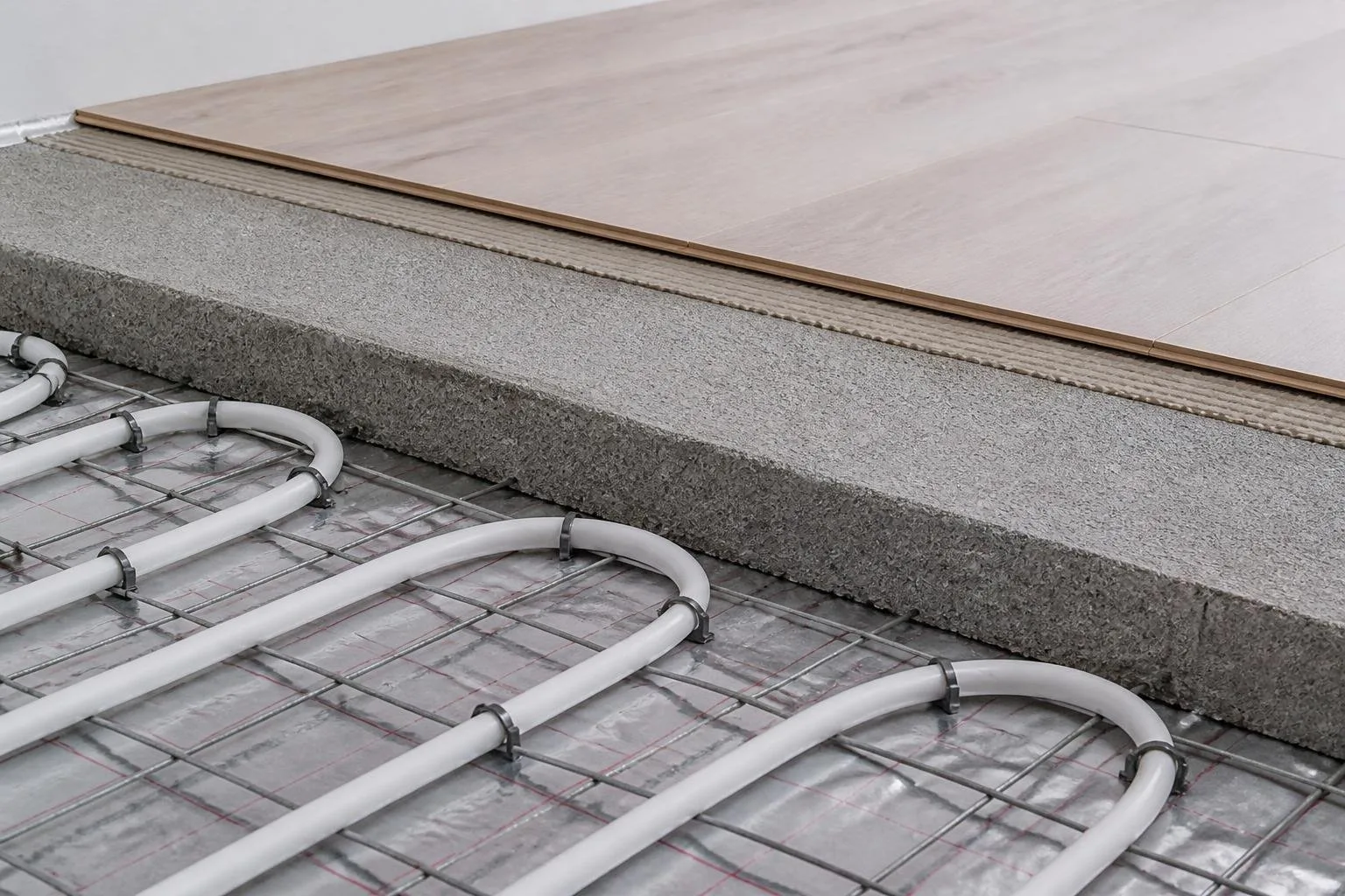 Fußbodenheizungsrohre neben Estrich und einem dünnen Bodenaufbau im Detail