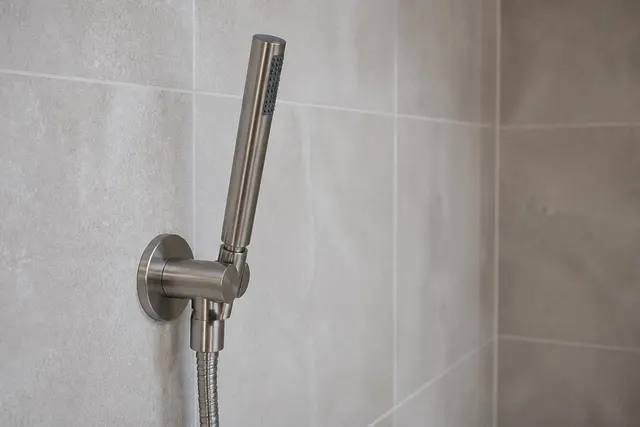 Wandanschluss mit integrierter Halterung für eine Handbrause an einer gefliesten Duschwand