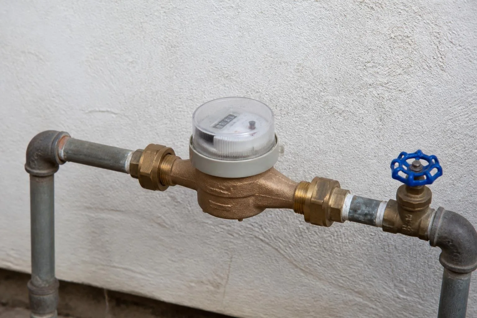 Wasserzähler mit sichtbarem Gehäuse und Rohranschlüssen in einer Hausinstallation